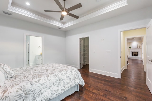 bedroom with dark wood-type flooring, ceiling fan, a tray ceiling, a closet, and a spacious closet