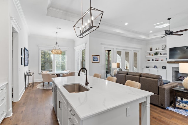 kitchen featuring light stone countertops, sink, decorative light fixtures, a center island with sink, and white cabinets