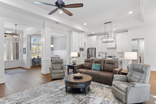 living room with ornate columns, a tray ceiling, ceiling fan, crown molding, and wood-type flooring