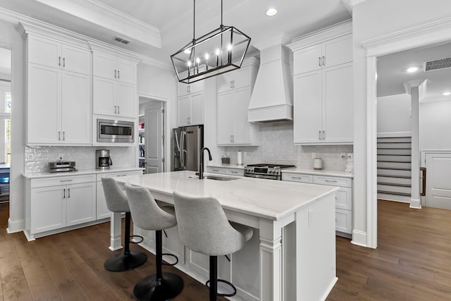 kitchen featuring white cabinets, custom exhaust hood, stainless steel appliances, and a kitchen island with sink