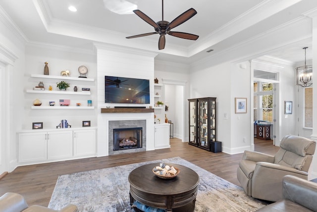 living room with a large fireplace, dark wood-type flooring, a raised ceiling, a chandelier, and ornamental molding