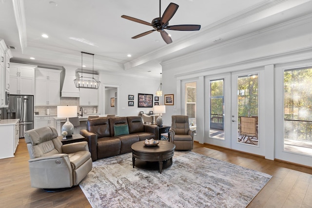 living room featuring ceiling fan, french doors, a raised ceiling, light wood-type flooring, and ornamental molding