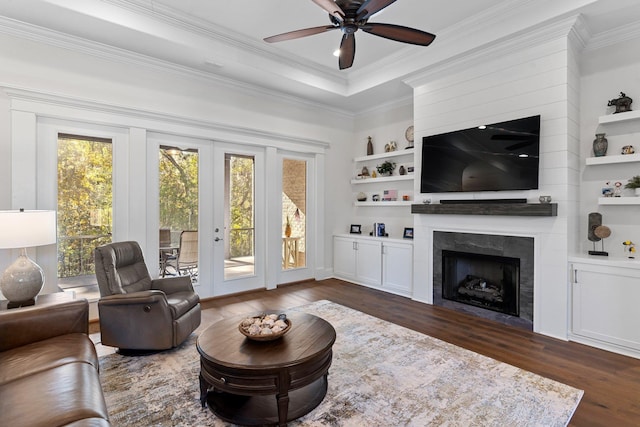 living room with dark wood-type flooring, french doors, crown molding, ceiling fan, and a fireplace