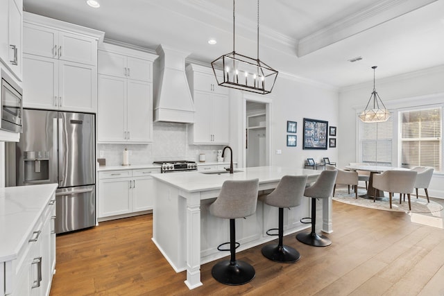 kitchen featuring a center island with sink, white cabinets, sink, custom range hood, and stainless steel appliances