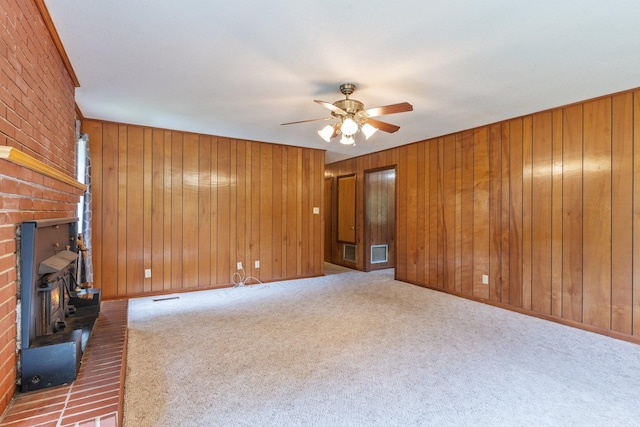 unfurnished living room with wood walls, ceiling fan, a wood stove, and dark carpet