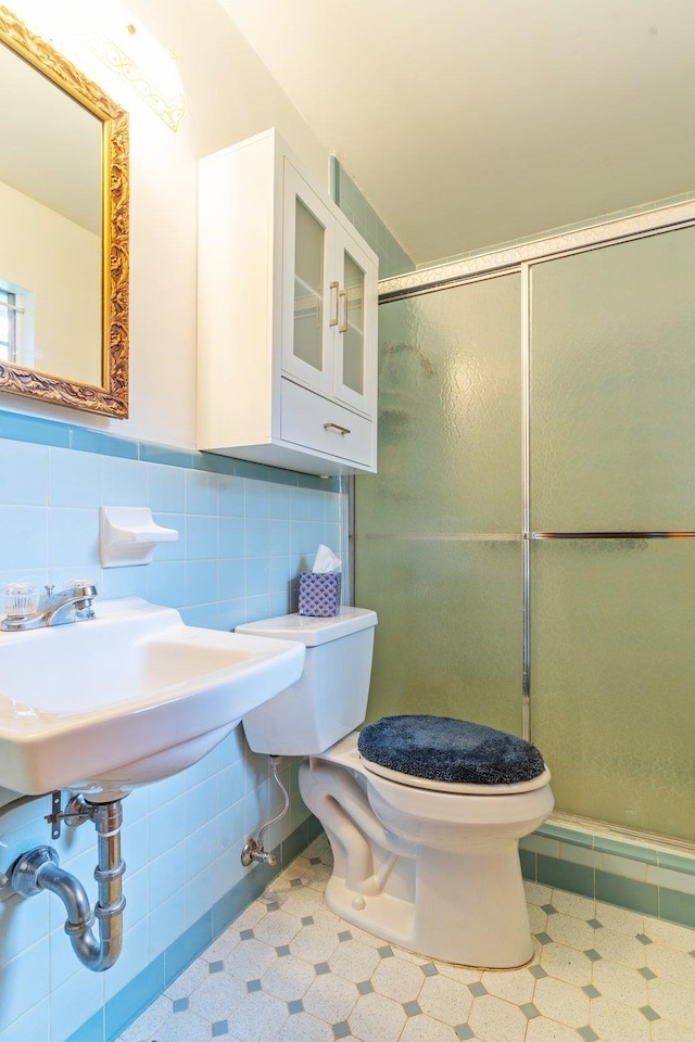 bathroom with toilet, tile walls, sink, and a shower with shower door