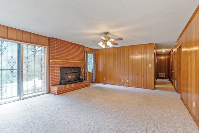 unfurnished living room with wooden walls, a textured ceiling, light carpet, and ceiling fan