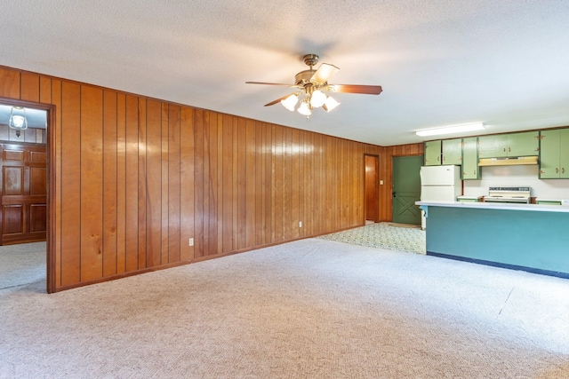 unfurnished living room featuring wooden walls, a textured ceiling, light colored carpet, and ceiling fan