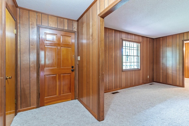 entrance foyer with wooden walls, a textured ceiling, and light carpet