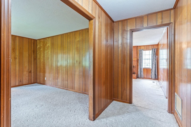 hallway featuring a textured ceiling, light colored carpet, and wooden walls