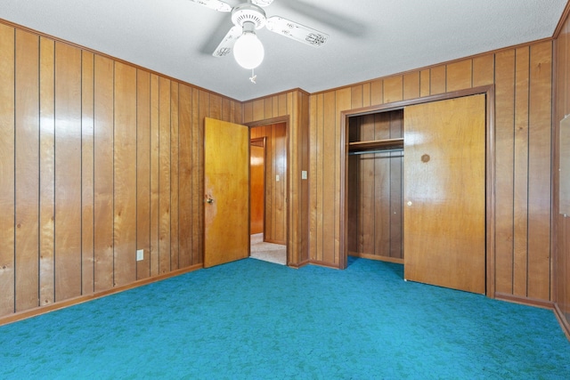 unfurnished bedroom with carpet floors, a textured ceiling, wooden walls, ceiling fan, and a closet