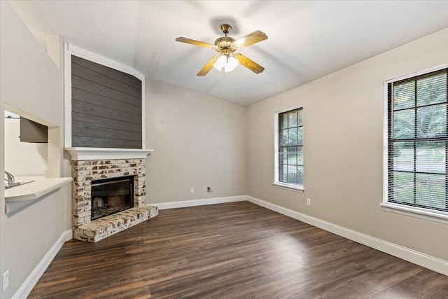 unfurnished living room featuring a brick fireplace, plenty of natural light, ceiling fan, and dark hardwood / wood-style flooring