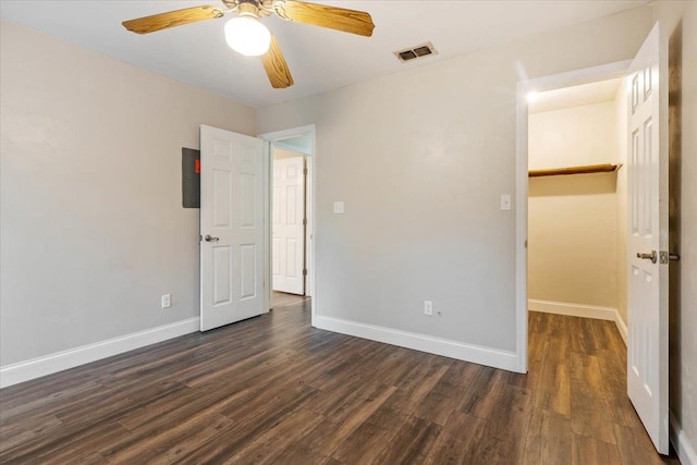 unfurnished bedroom with dark wood-type flooring, ceiling fan, a walk in closet, and a closet