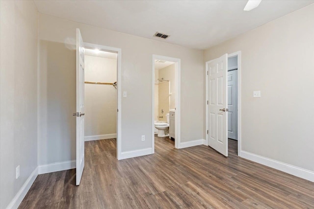 unfurnished bedroom with dark wood-type flooring, connected bathroom, ceiling fan, a closet, and a walk in closet