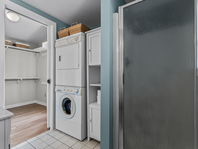 clothes washing area with baseboards, stacked washer and dryer, cabinet space, and light tile patterned floors
