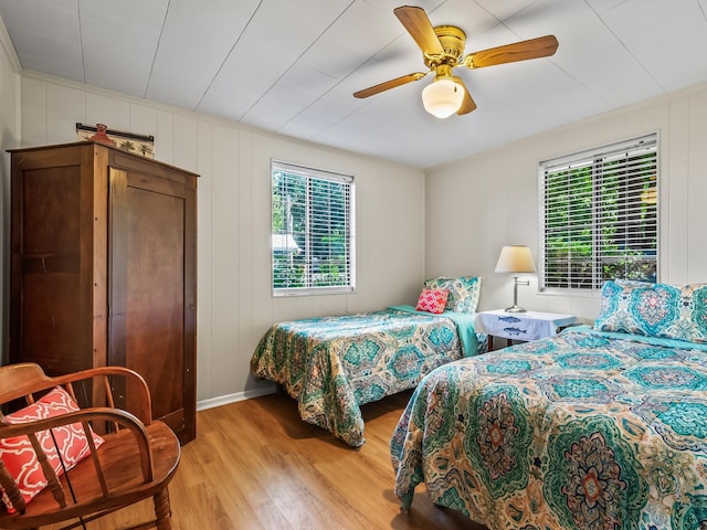 bedroom featuring baseboards, a ceiling fan, light wood finished floors, and multiple windows