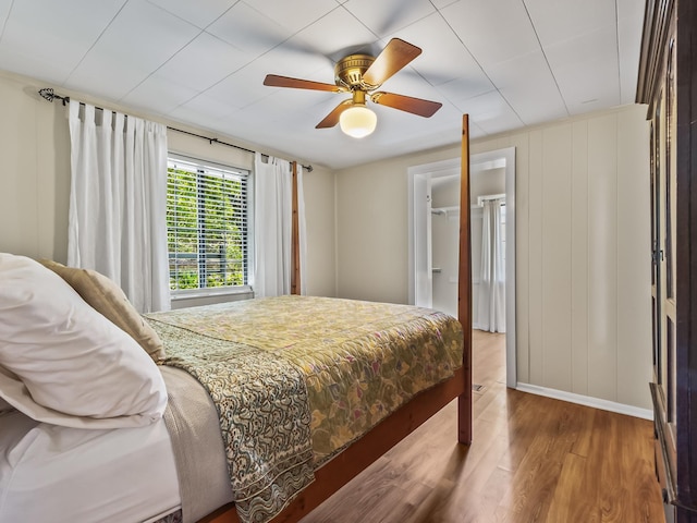 bedroom featuring ceiling fan, baseboards, wood finished floors, a spacious closet, and a closet