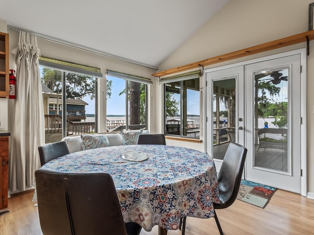 dining room with french doors, light wood-style flooring, a water view, and lofted ceiling