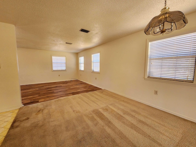 carpeted spare room featuring tile patterned flooring, visible vents, and a textured ceiling