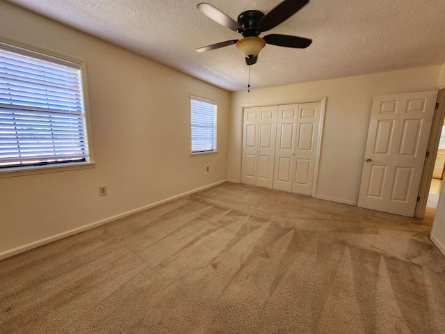 unfurnished bedroom with light carpet, baseboards, a ceiling fan, a textured ceiling, and a closet