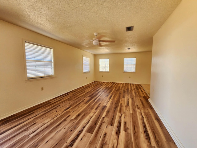 unfurnished room with baseboards, visible vents, a ceiling fan, wood finished floors, and a textured ceiling