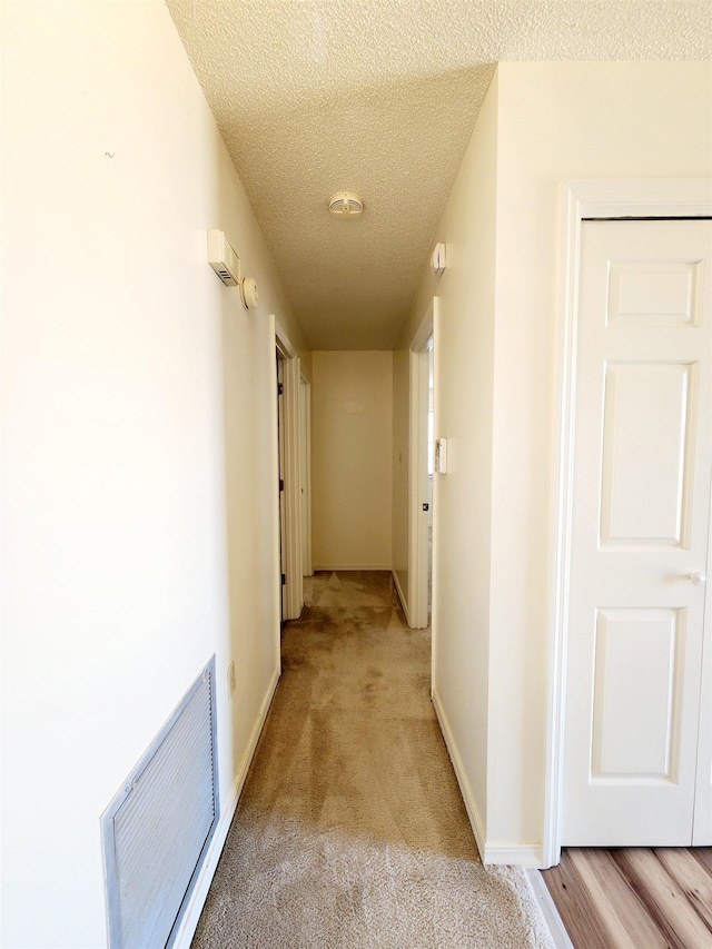 hall with light carpet, visible vents, a textured ceiling, and baseboards