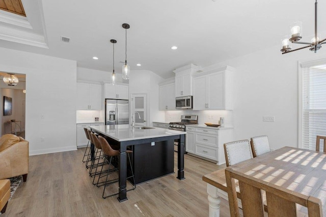 kitchen featuring light wood-type flooring, appliances with stainless steel finishes, a kitchen bar, hanging light fixtures, and a kitchen island with sink