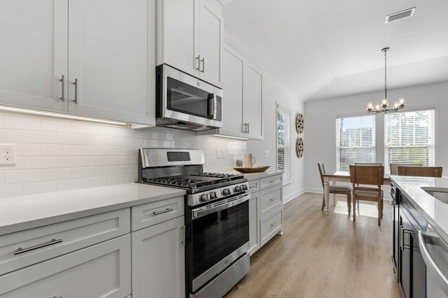 kitchen with tasteful backsplash, stainless steel appliances, light wood-type flooring, white cabinetry, and hanging light fixtures