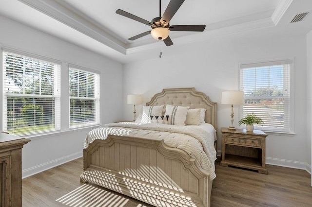 bedroom with hardwood / wood-style flooring, ceiling fan, crown molding, and a tray ceiling