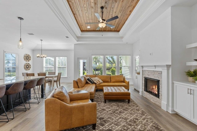 living room featuring a stone fireplace, light wood-type flooring, a raised ceiling, wood ceiling, and ceiling fan with notable chandelier