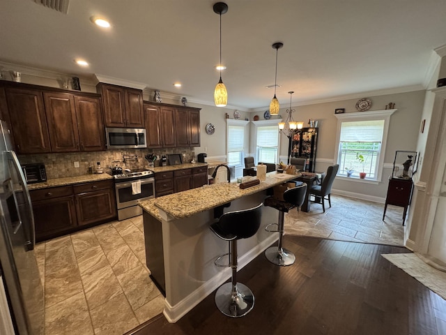 kitchen with ornamental molding, decorative backsplash, light stone countertops, dark brown cabinets, and stainless steel appliances