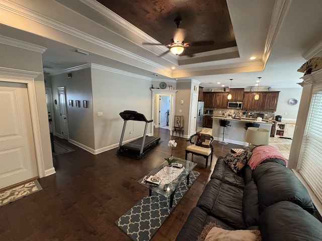 living room with crown molding, dark wood finished floors, a ceiling fan, baseboards, and a tray ceiling