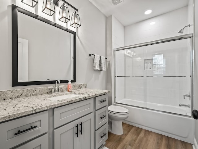 full bathroom with shower / bath combination with glass door, hardwood / wood-style floors, vanity, and toilet