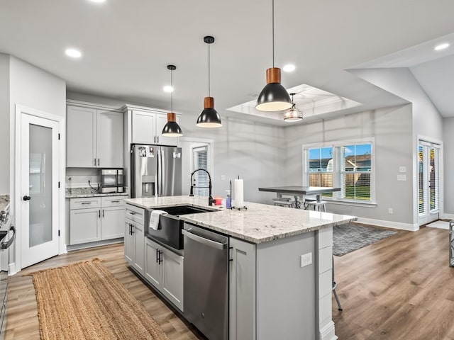 kitchen with sink, hanging light fixtures, light stone countertops, an island with sink, and stainless steel appliances