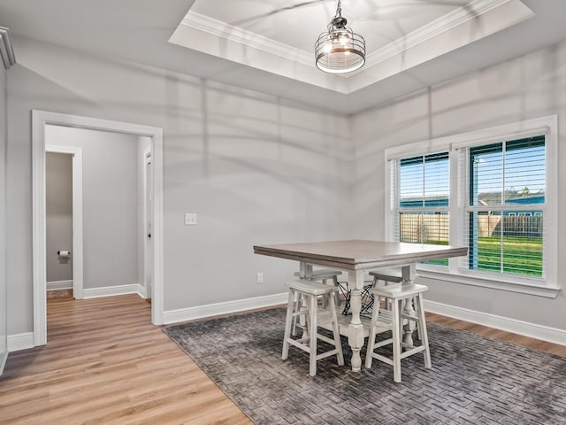 dining room with a raised ceiling, wood-type flooring, and ornamental molding