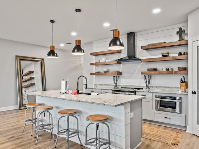 kitchen with pendant lighting, wall chimney exhaust hood, white cabinetry, and appliances with stainless steel finishes