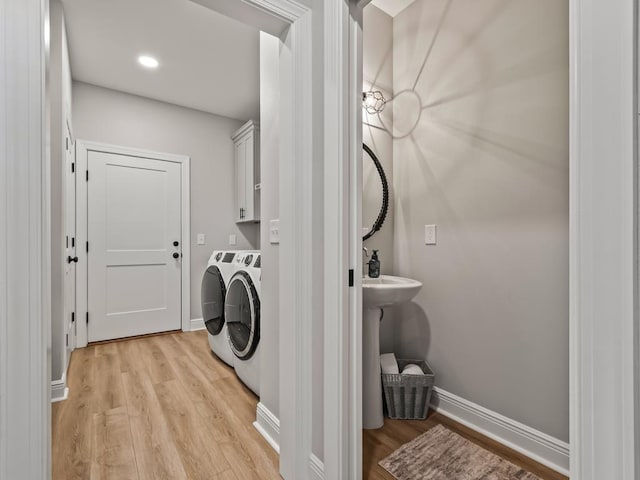 laundry room with separate washer and dryer, cabinets, and light hardwood / wood-style floors