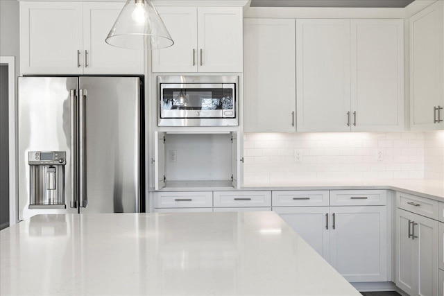 kitchen with backsplash, appliances with stainless steel finishes, white cabinets, and decorative light fixtures