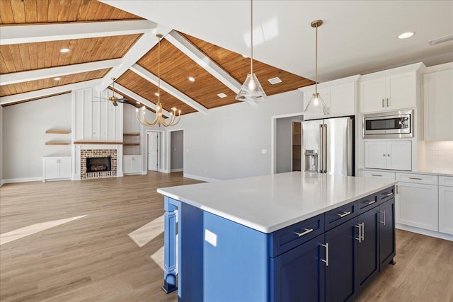 kitchen featuring tasteful backsplash, stainless steel appliances, blue cabinets, pendant lighting, and white cabinetry