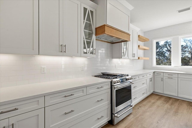 kitchen featuring stainless steel range with gas cooktop, white cabinetry, decorative backsplash, and light hardwood / wood-style flooring