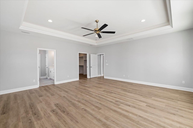 unfurnished bedroom with light wood-type flooring, a raised ceiling, and a spacious closet