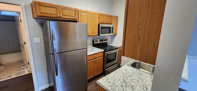 kitchen with sink, light stone counters, stainless steel appliances, and dark wood-type flooring