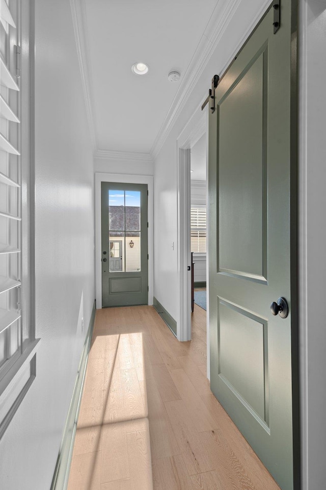 doorway to outside with ornamental molding, light wood-style flooring, baseboards, and a barn door