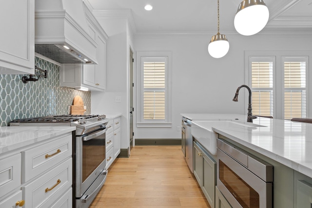 kitchen with custom range hood, appliances with stainless steel finishes, hanging light fixtures, crown molding, and a sink