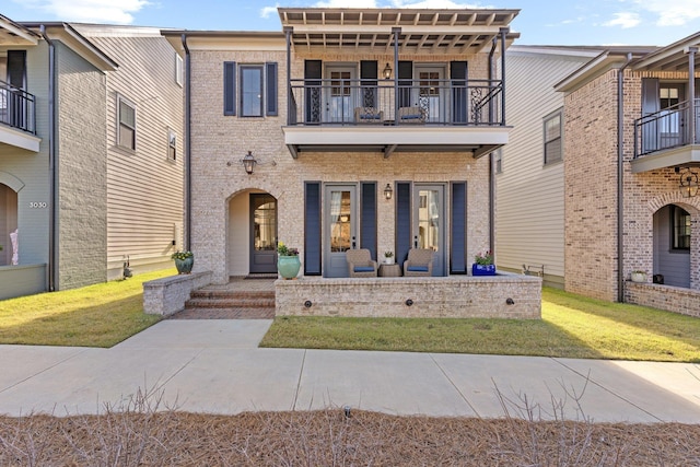 view of front of home featuring a balcony, covered porch, a front yard, and brick siding