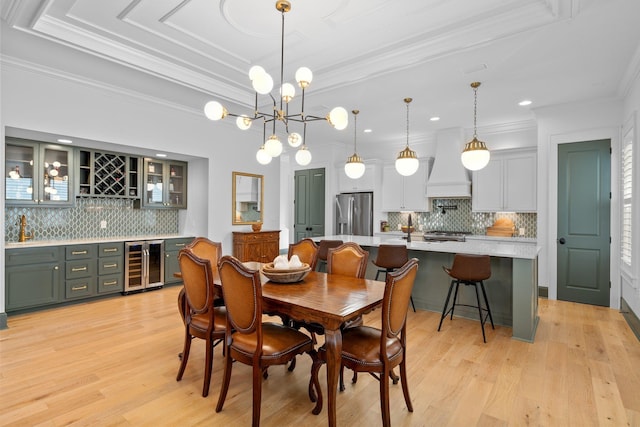 dining room featuring beverage cooler, a raised ceiling, indoor bar, light wood-style flooring, and ornamental molding