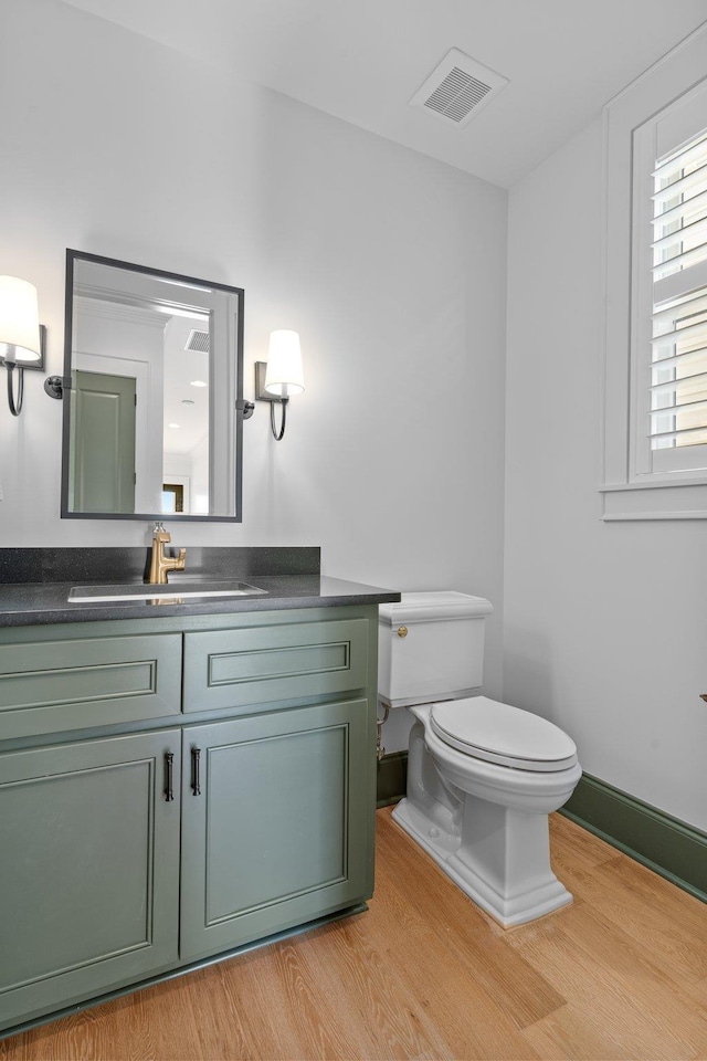 half bathroom with toilet, wood finished floors, and visible vents