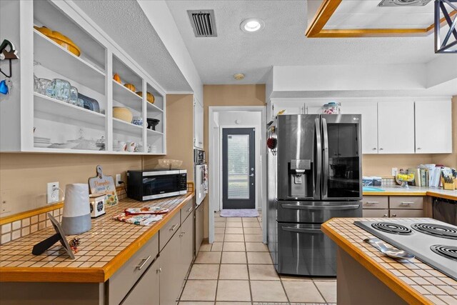 310 Glenridge Rd, Perry, FL 32348 - kitchen featuring stainless steel appliances, tile countertops, white cabinetry, a textured ceiling, and light tile patterned floors