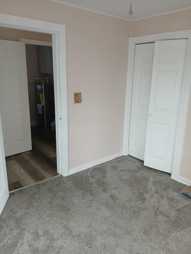 unfurnished bedroom with a closet, crown molding, water heater, and carpet