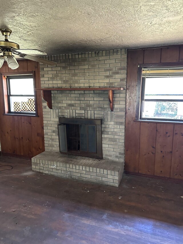 unfurnished living room with a ceiling fan, wooden walls, wood finished floors, a textured ceiling, and a brick fireplace